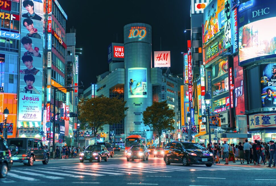 Cars driving through a neon-lit intersection in Shibuya, Tokyo, at night