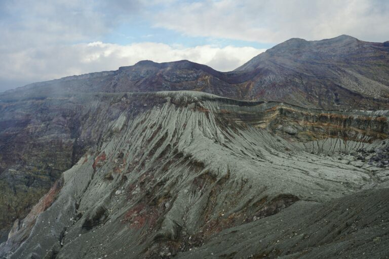 Rugged volcanic crater with steep, eroded slopes and cloudy sky