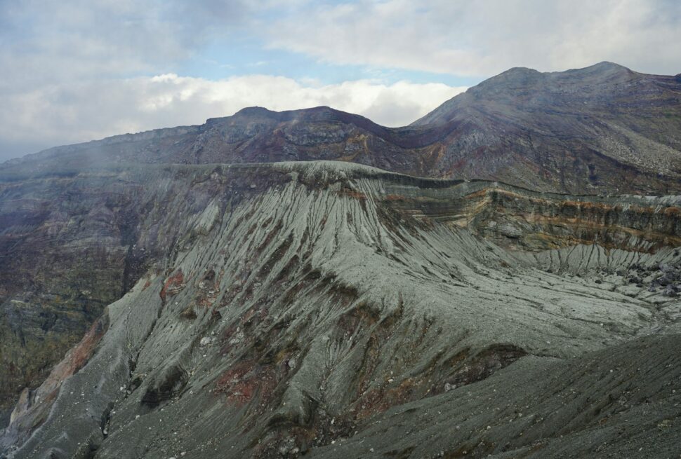 Rugged volcanic crater with steep, eroded slopes and cloudy sky