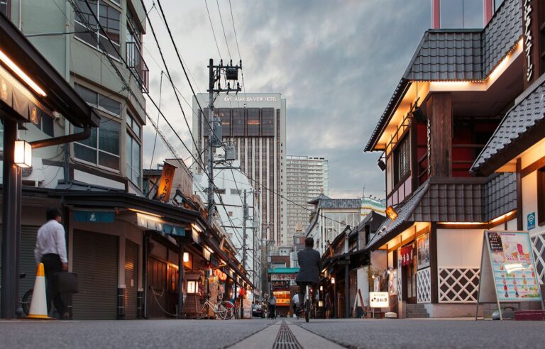 A person cycling down a street in Asakusa with traditional buildings and a hotel