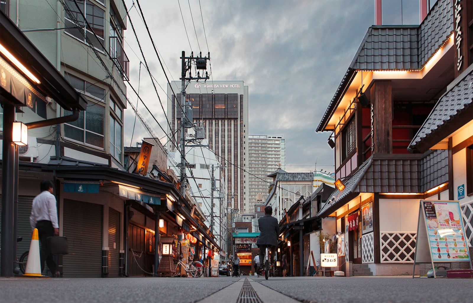 A person cycling down a street in Asakusa with traditional buildings and a hotel