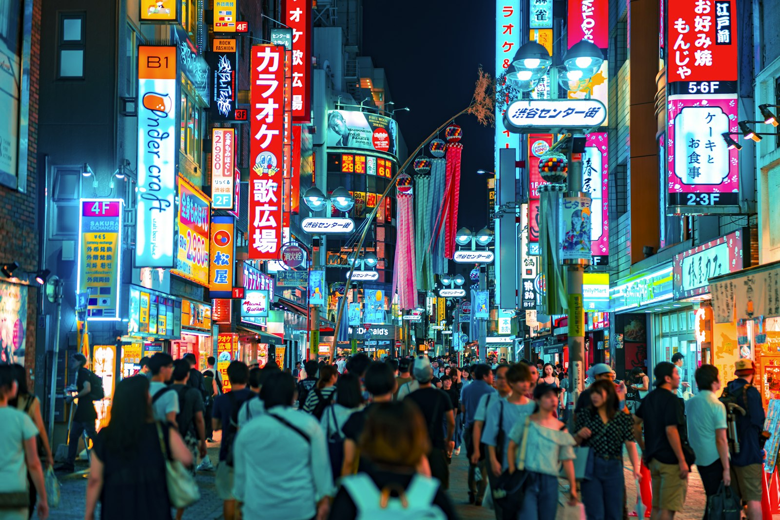 A crowd of people walking down a neon-lit street in Shibuya, Tokyo