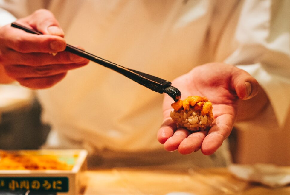 person holding black chopsticks with brown food